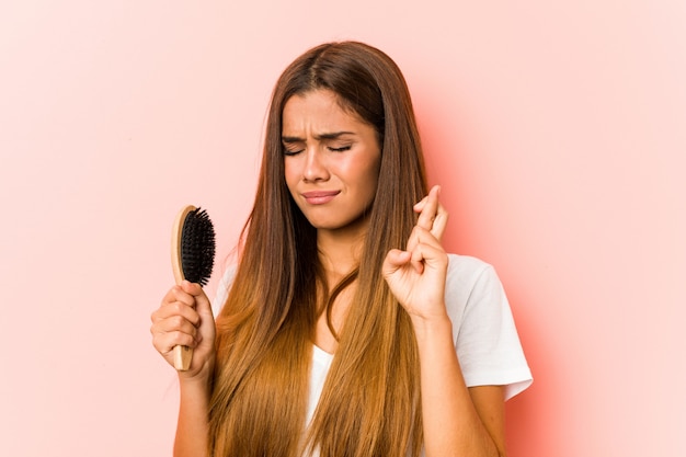 Young caucasian woman holding an hairbrush crossing fingers