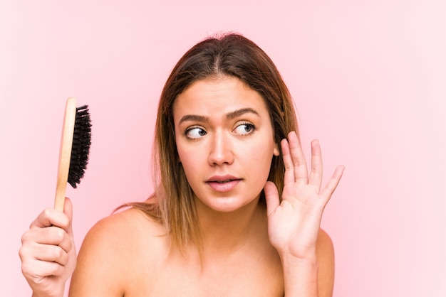 Young caucasian woman holding a hairbrush isolated trying to listening a gossip.