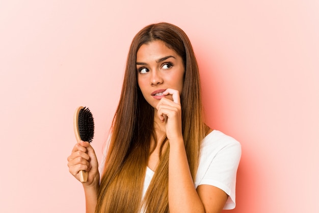 Young caucasian woman holding an hairbrush relaxed thinking about something looking at a blank space.