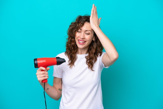 青い背景で隔離のヘアドライヤーを保持している若い白人女性は何かを実現し、解決策を意図しています