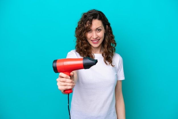 幸せな表情で青い背景で隔離のヘアドライヤーを保持している若い白人女性