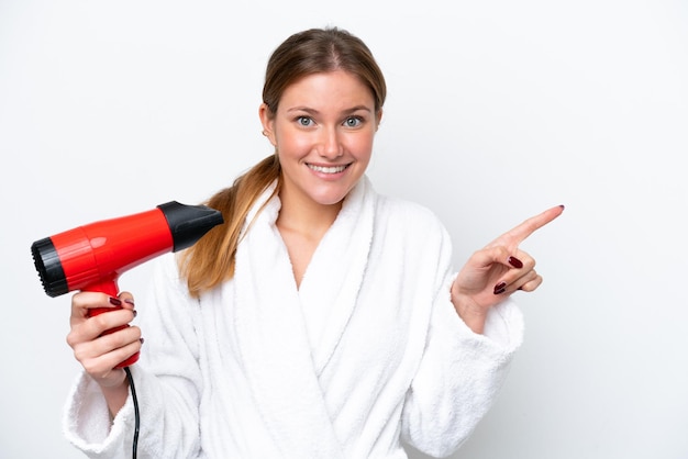 Young caucasian woman holding hairdryer isolated on white background surprised and pointing finger to the side