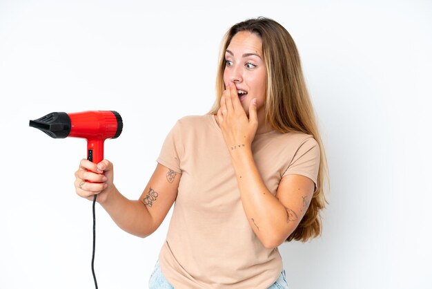 Young caucasian woman holding a hairdryer isolated on white background with surprise and shocked facial expression