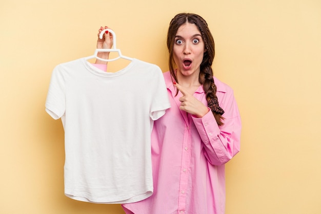 Photo young caucasian woman holding a hanger isolated on yellow background pointing to the side