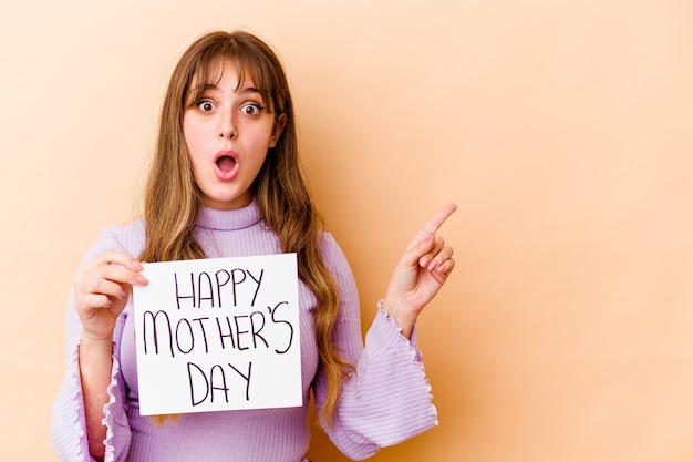 Young caucasian woman holding a Happy mothers day placard isolated pointing to the side
