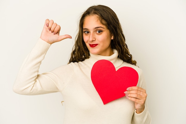 Young caucasian woman holding a heart valentines day shape isolated feels proud and self confident, example to follow.