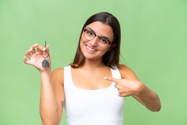 Young caucasian woman holding home keys isolated on green chroma background with surprise facial expression