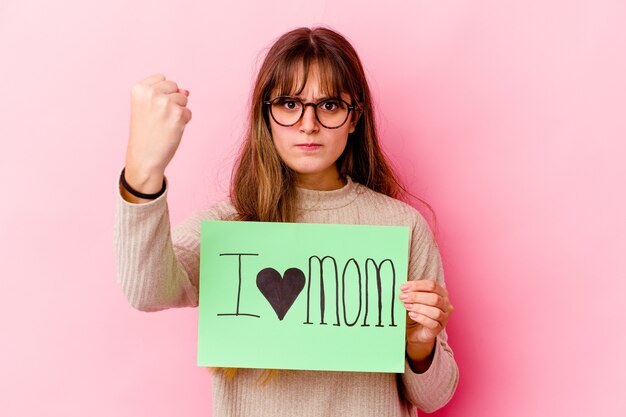 Young caucasian woman holding a I love mom isolated showing fist, aggressive facial expression.