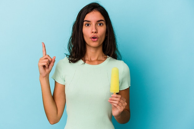 Giovane donna indoeuropea in possesso di un gelato isolato su sfondo blu giovane donna indoeuropea in possesso di un gelato isolato su sfondo blu con qualche grande idea, concetto di creatività.