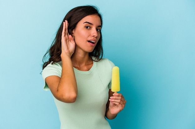 Young caucasian woman holding an ice cream isolated on blue background Young caucasian woman holding an ice cream isolated on blue background trying to listening a gossip.