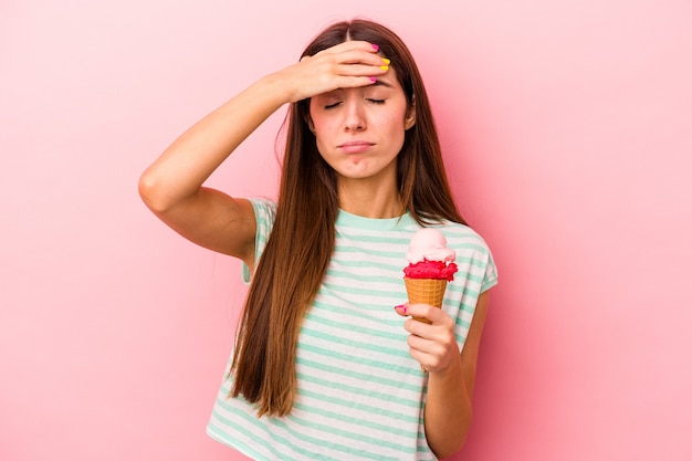 Young caucasian woman holding an ice cream isolated on pink background being shocked, she has remembered important meeting.