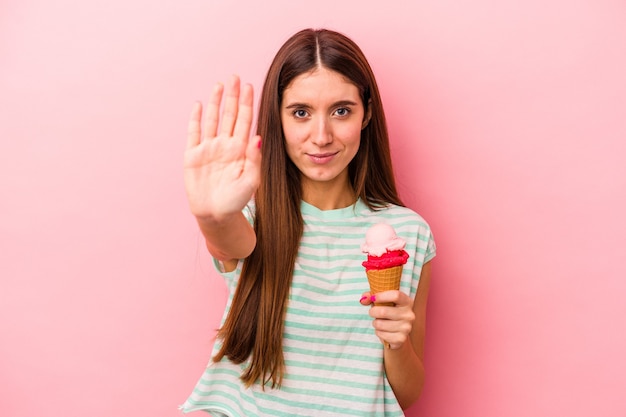 Young caucasian woman holding an ice cream isolated on pink background standing with outstretched hand showing stop sign, preventing you.