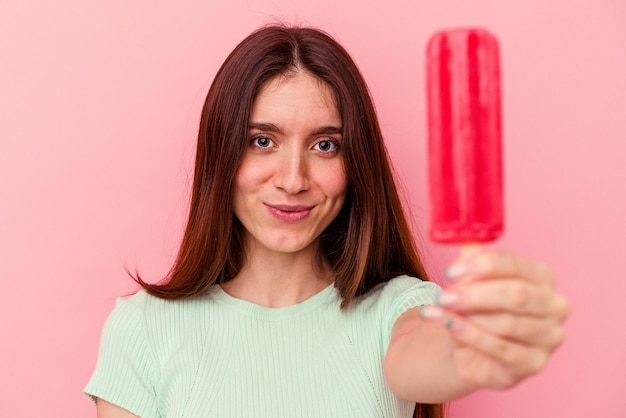 Young caucasian woman holding an ice cream isolated on pink background