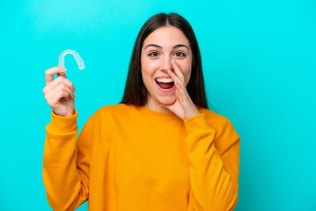 Young caucasian woman holding invisible braces isolated on blue background shouting with mouth wide open