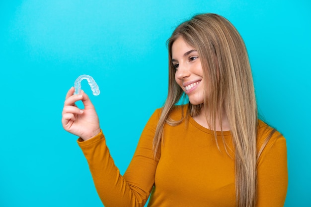 Young caucasian woman holding invisible braces isolated on blue background with happy expression