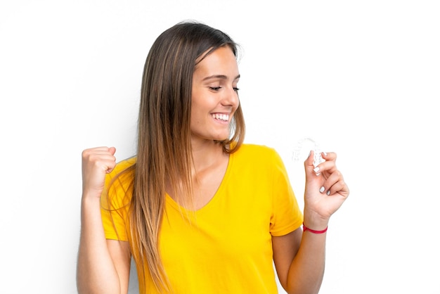 Young caucasian woman holding invisible braces isolated on white background celebrating a victory