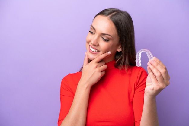 Young caucasian woman holding invisible braces thinking an idea\
and looking side