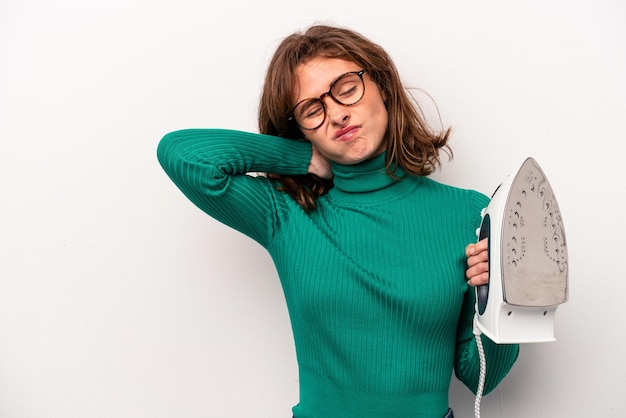 Young caucasian woman holding iron isolated on white background touching back of head thinking and making a choice