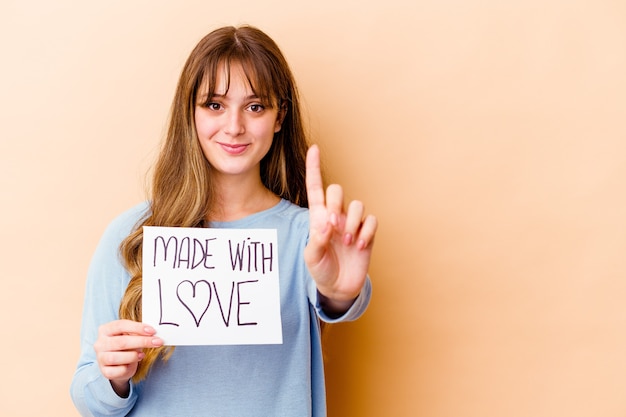 Young caucasian woman holding a made with love placard isolated showing number one with finger.