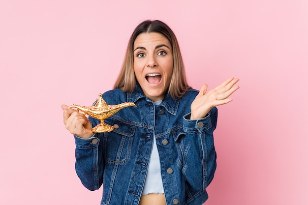 Giovane donna caucasica che tiene una lampada magica che celebra una vittoria o un successo