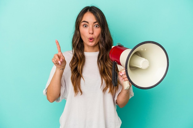 Young caucasian woman holding a megaphone isolated on blue\
background having some great idea, concept of creativity.