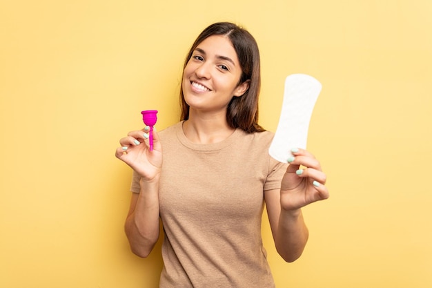 Young caucasian woman holding a menstrual cup isolated on yellow background