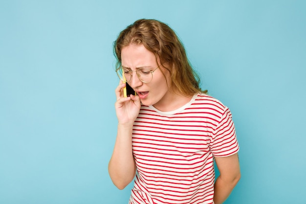 Giovane donna caucasica in possesso di telefono cellulare isolato su sfondo blu