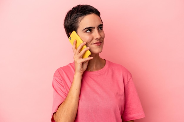 Young caucasian woman holding mobile phone isolated on pink background