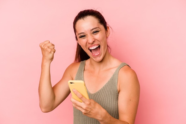 Young caucasian woman holding mobile phone isolated on pink background