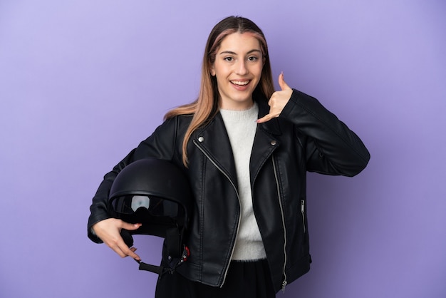 Young caucasian woman holding a motorcycle helmet isolated on purple background making phone gesture. Call me back sign