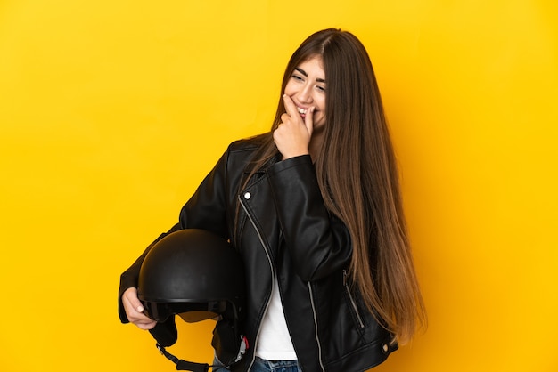 Young caucasian woman holding a motorcycle helmet isolated on yellow wall laughing