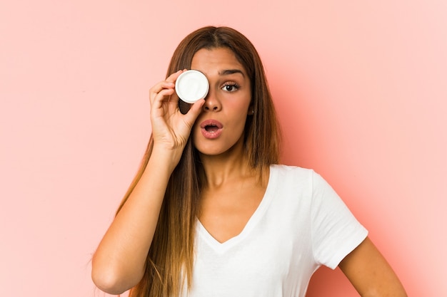 Photo young caucasian woman holding a mousturizer isolated on a pink wall