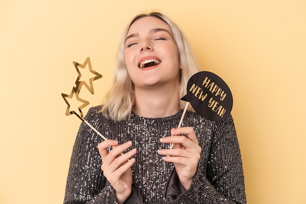 Young caucasian woman holding new year props isolated on yellow background