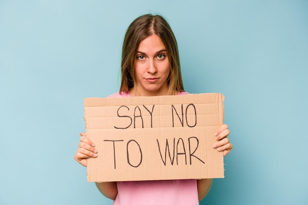 Young caucasian woman holding no war placard isolated on blue background