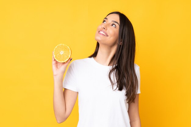 Young caucasian woman holding an orange isolated on yellow