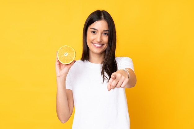 Young caucasian woman holding an orange isolated on yellow