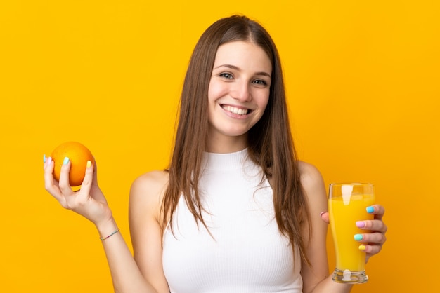 Молодая кавказская женщина держа апельсин на оранжевой стене