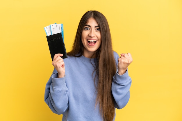 Young caucasian woman holding a passport isolated on yellow background celebrating a victory in winner position