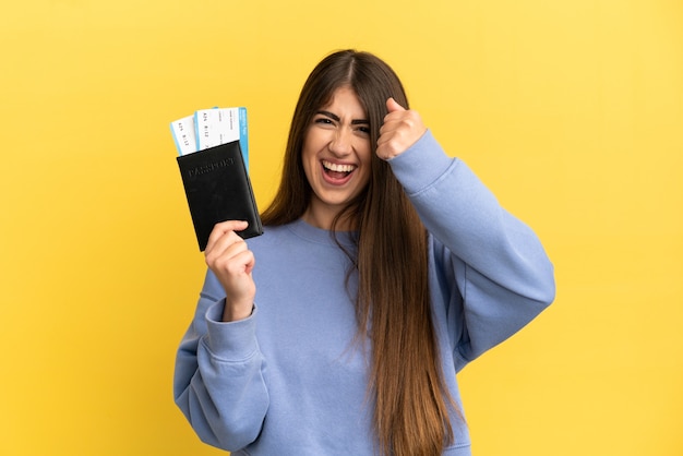 Young caucasian woman holding a passport isolated on yellow background celebrating a victory