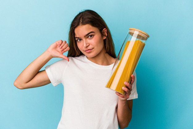 Young caucasian woman holding a pasta jar isolated on blue background showing a dislike gesture, thumbs down. Disagreement concept.