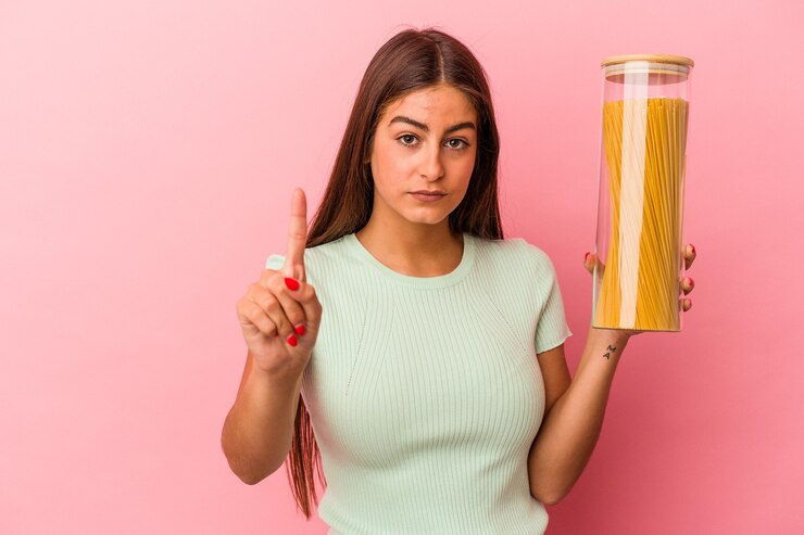 फोटो young caucasian woman holding a pasta jar isolated on pink background showing number one with finger.
