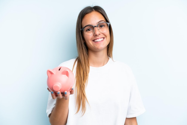 Young caucasian woman holding a piggybank isolated on blue background smiling a lot