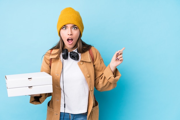 Young caucasian woman holding pizzas isolated pointing to the side