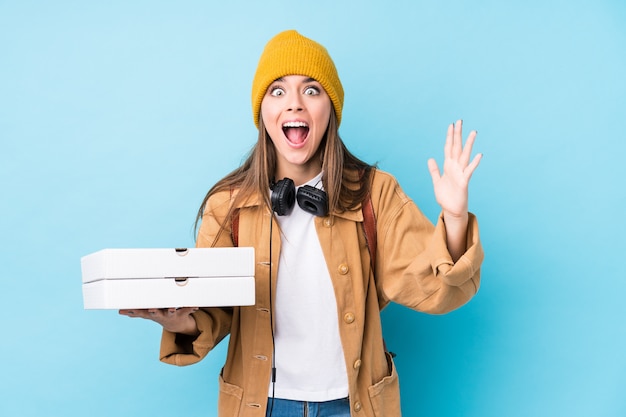 Young caucasian woman holding pizzas isolated receiving a pleasant surprise, excited and raising hands.
