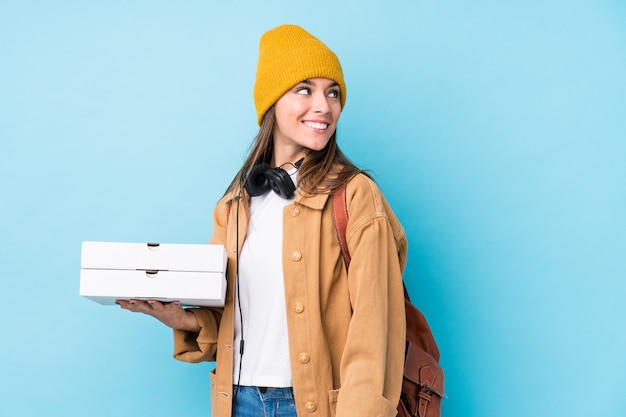 Young caucasian woman holding pizzas looks aside smiling, cheerful and pleasant.