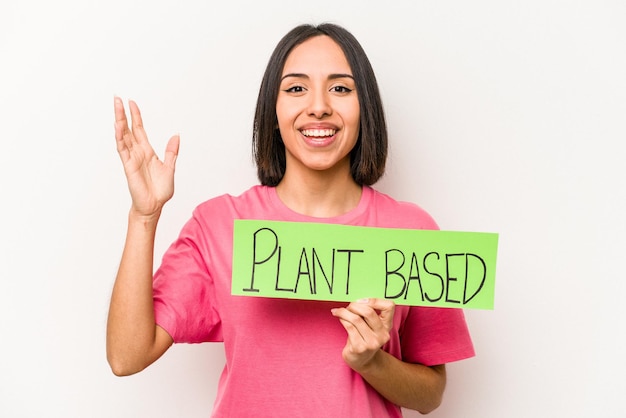 Young caucasian woman holding plant based placard isolated on white background receiving a pleasant surprise excited and raising hands