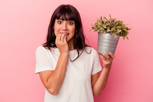 Young caucasian woman holding a plant isolated on pink background biting fingernails, nervous and very anxious.