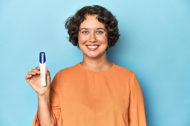 Young Caucasian woman holding a pregnancy test studio blue background