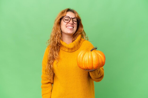 Young caucasian woman holding a pumpkin isolated on green screen chroma key background laughing