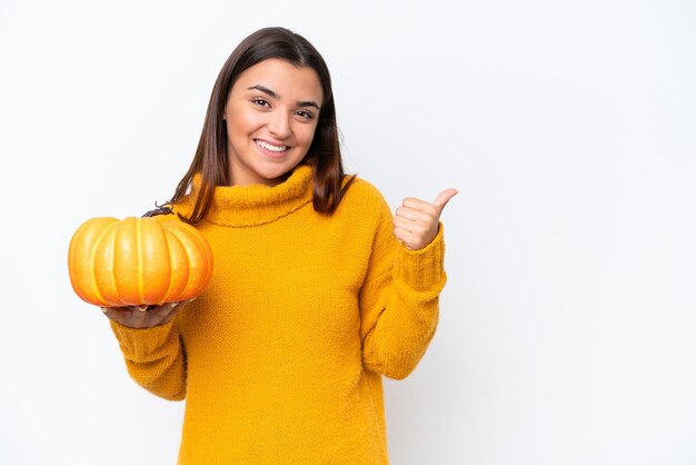 Foto giovane donna caucasica che tiene una zucca isolata su sfondo bianco che indica il lato per presentare un prodotto